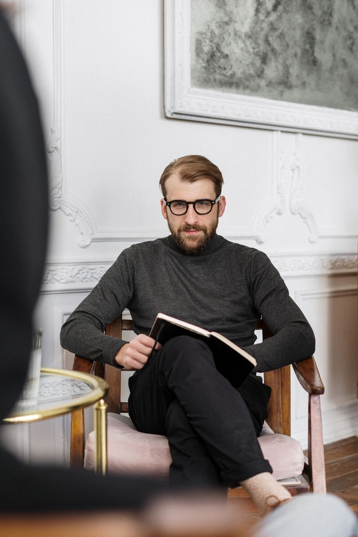 A therapist holding a book, seated in a modern office during a counseling session.